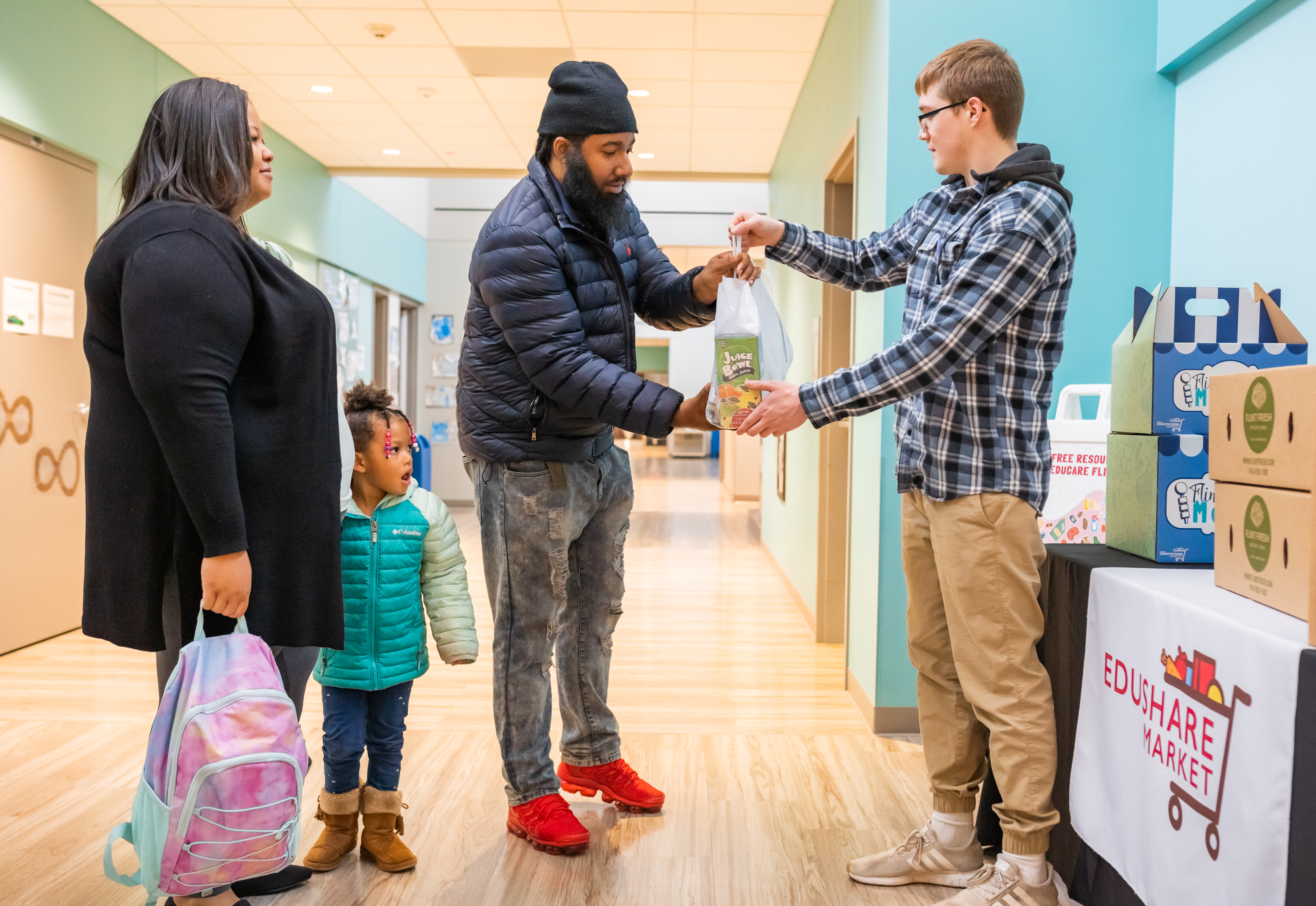 A father is handed a meal in a bag from a volunteer. The mother and child stand next to them.