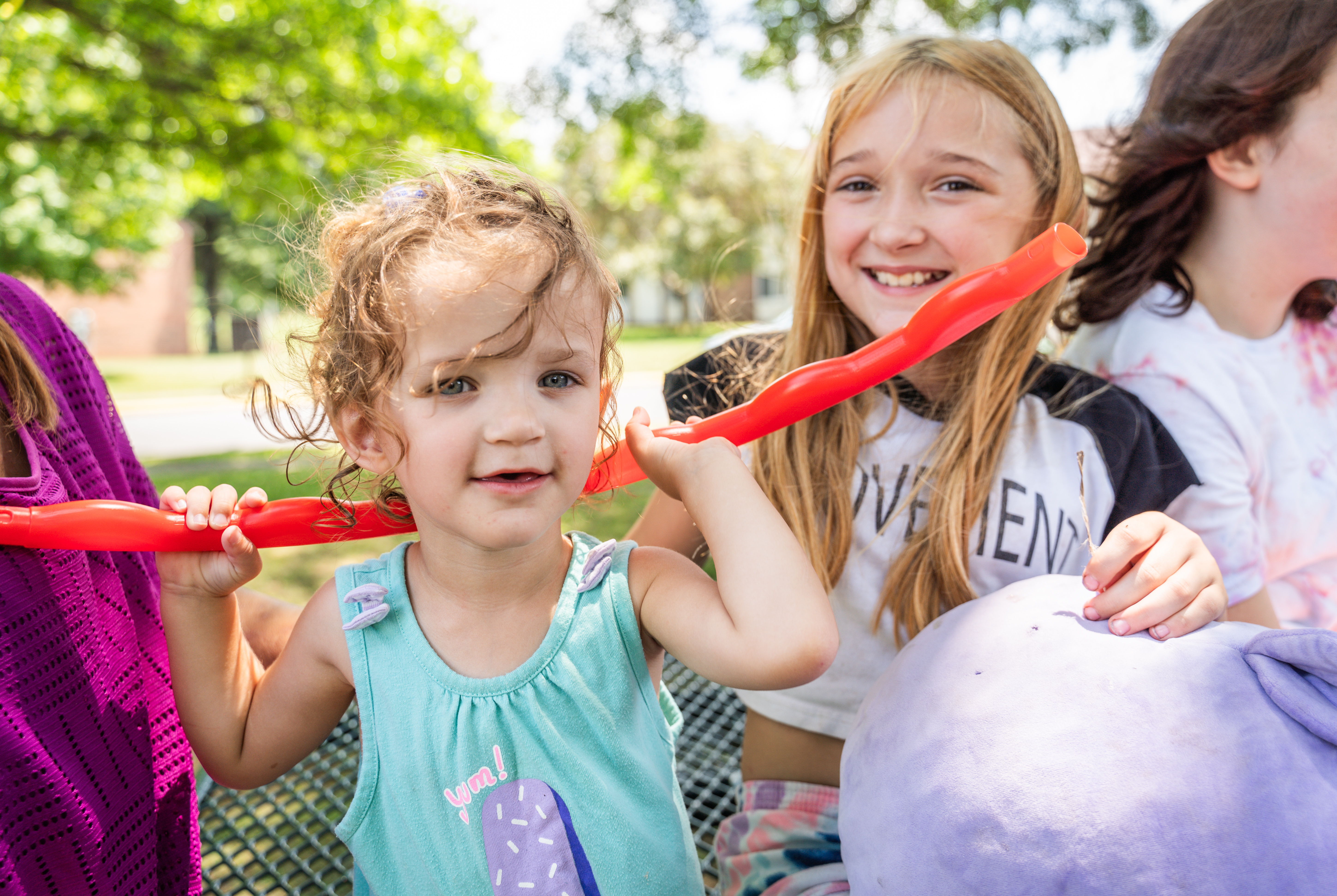 two young girls play outside during the summer with a red rope. 