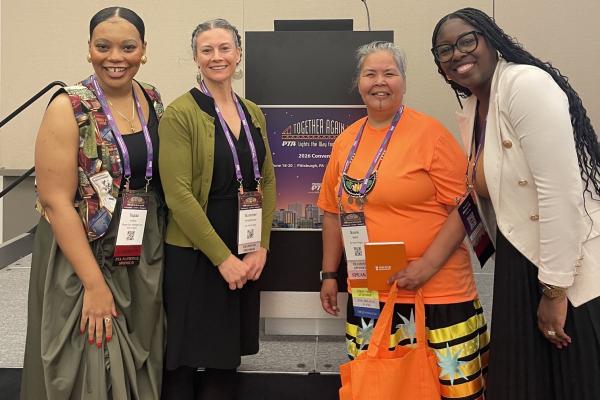 Topaz, Chioma, Bewaush, and Summer taking a picture in front of a podium at the PTA conference